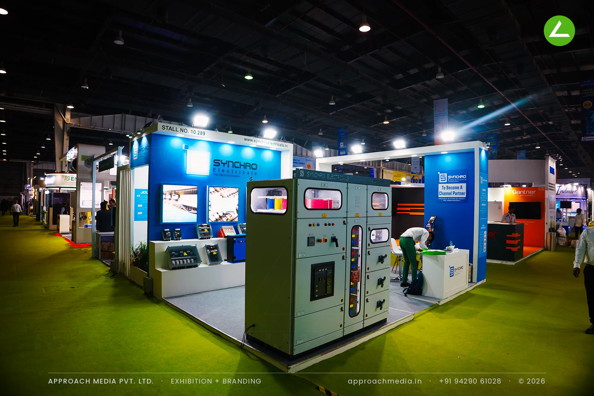 A live LT switchgear panel at the open corner of Synchro Electricals' stall, with product counters and two screens behind.