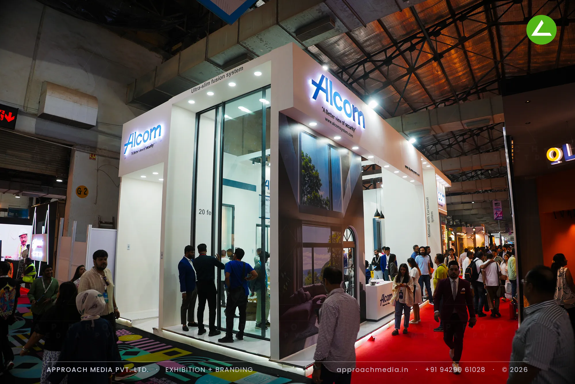 Visitors at Alcom's ACETECH stand, where full-height glazed window systems sit in white bays under a backlit brand logo.
