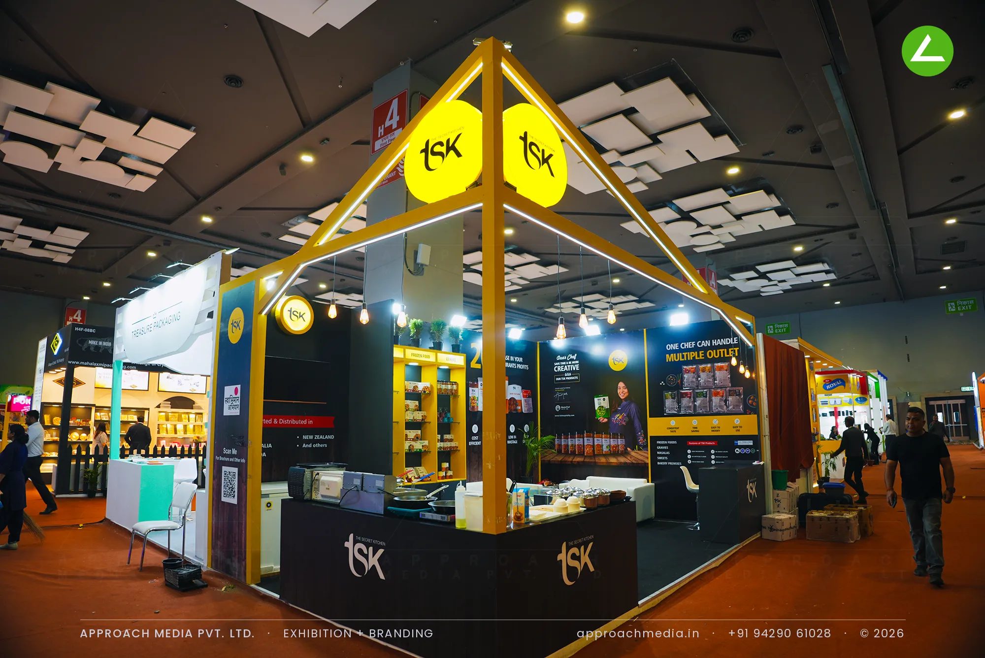 Two backlit circular TSK logo discs at the apex of a yellow portal frame, above charcoal shelving bays of packs and jars.