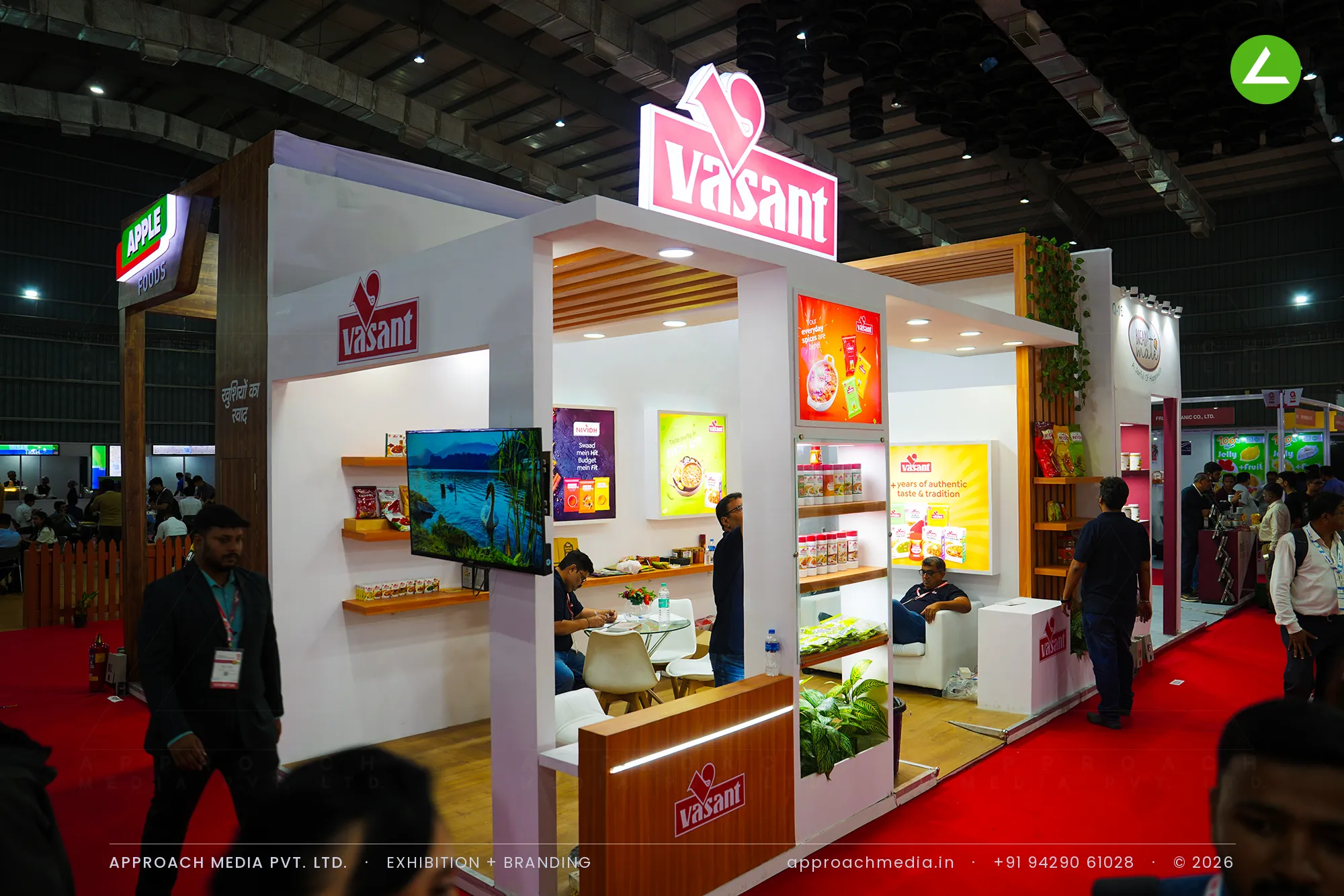 A raised red Vasant logo box above teak floating shelves, backlit food graphics and an LED-lit wood reception counter.