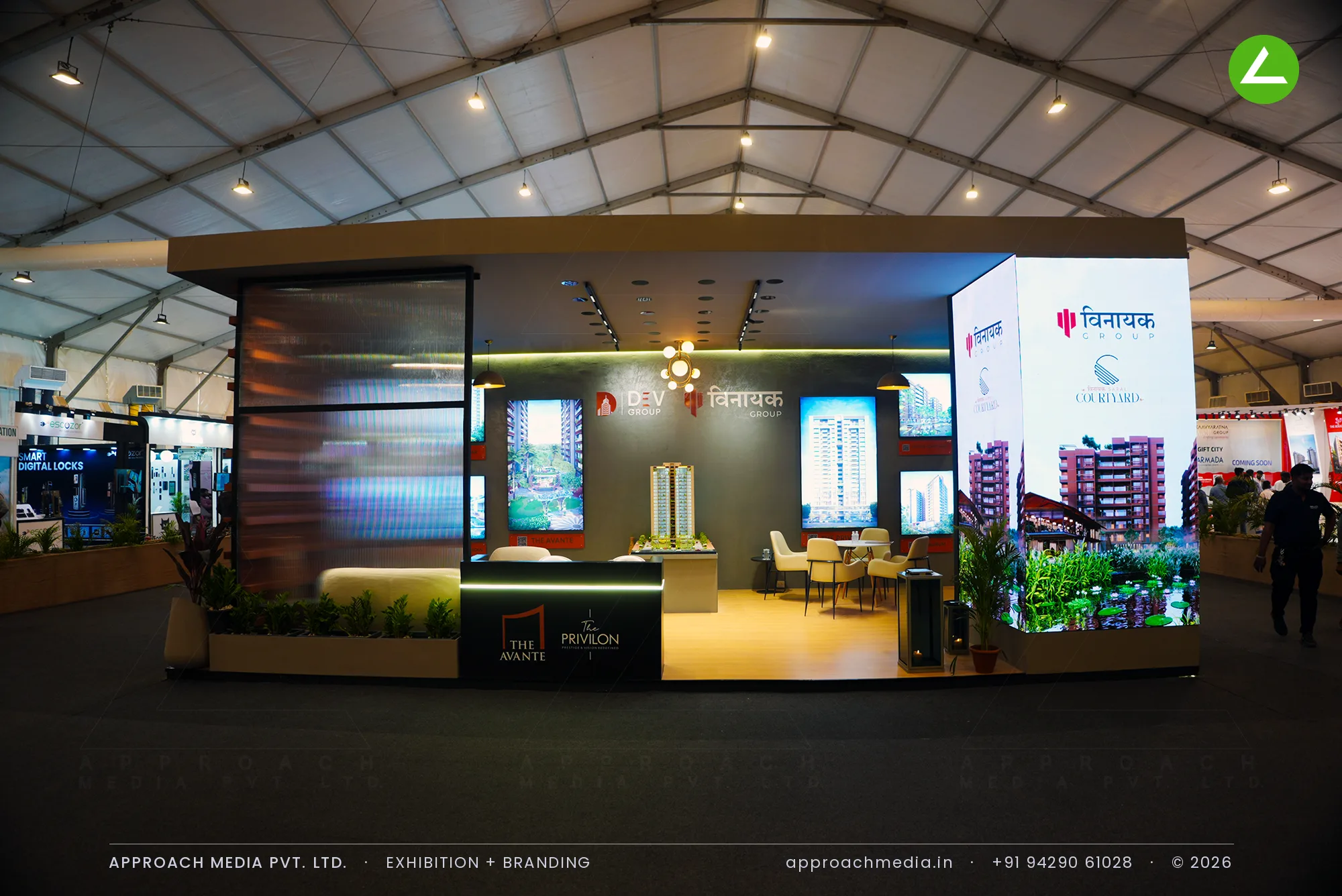 Dev Group and Vinayak Group's dark olive stall at the Tricity Property Expo, with a lit scale model and a jali screen