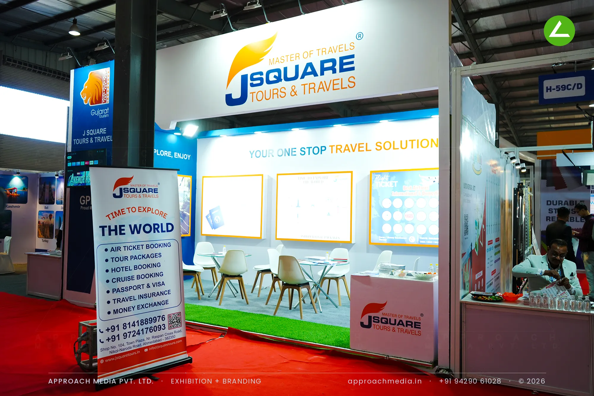J Square Tours & Travels exhibition stall design at GPBS Gandhinagar with a blue back wall and orange-framed travel panels