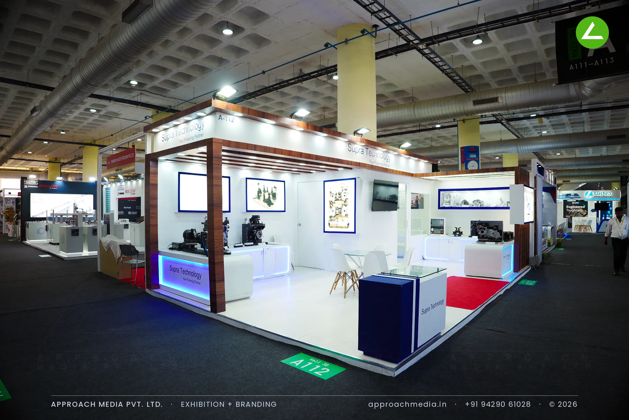 Supra Technology exhibition stall design at IMTEX Bengaluru with white counters, blue cove lighting and walnut rafters