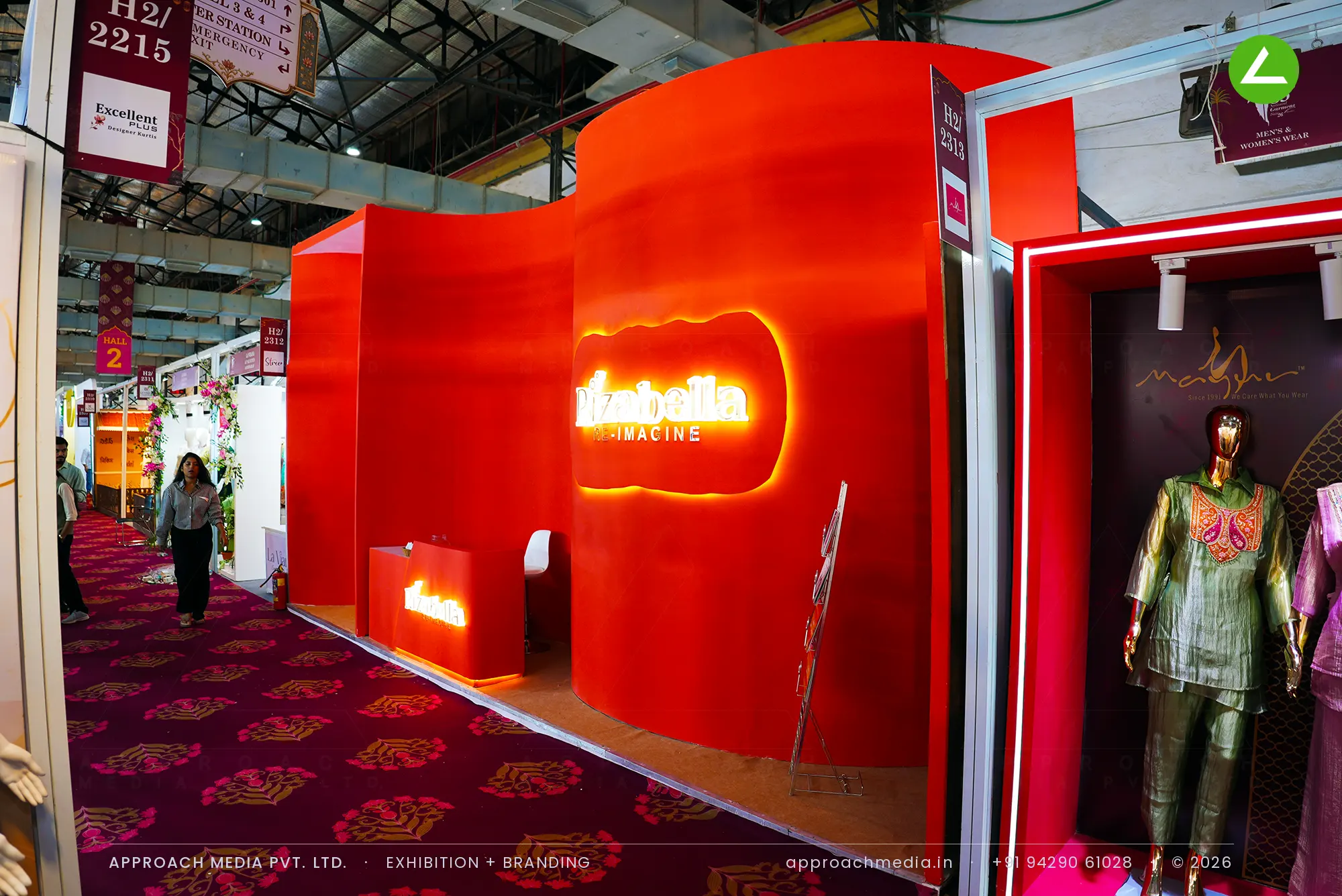 Curved red frontage with halo-lit logo — exhibition stall design at National Garment Fair Mumbai for Rizabella